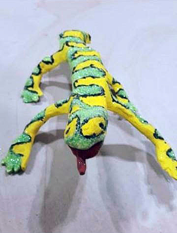 A yellow & green billowing patterned ceramic sculpture of a lizard with its tongue sticking out, painted with acrylic paint and glitter