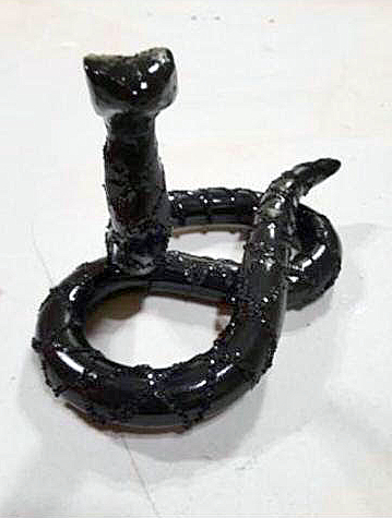 A ceramic sculpture of a black mamba snake coiled and raised, painted with gloss and black glitter