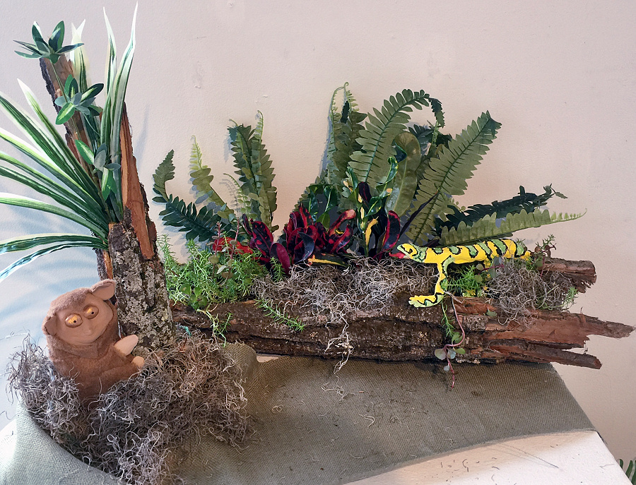 Frontispiece, floral and plant arrangement with wood log planter, ceramic lizard, and ceramic tarsier monkey.