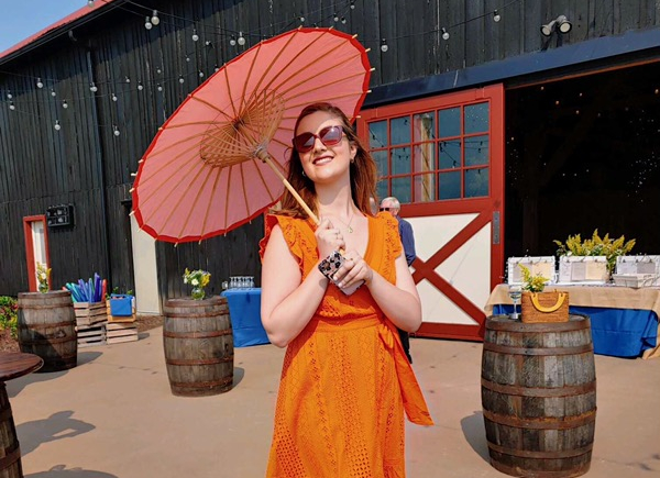 Emma Farnham outdoors wearing an orange dress and holding a parasol